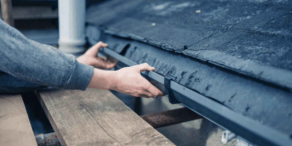 A technician examines a gutter, highlighting the importance of regular maintenance to identify signs your gutter needs repair.
