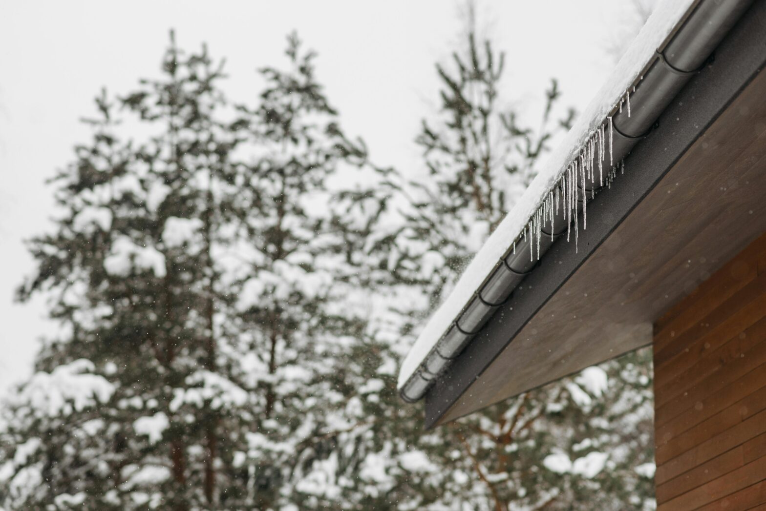 Snow-covered roof with icicles hanging from the gutters, highlighting the importance of proper gutter installation in NJ during winter to prevent ice buildup and damage.